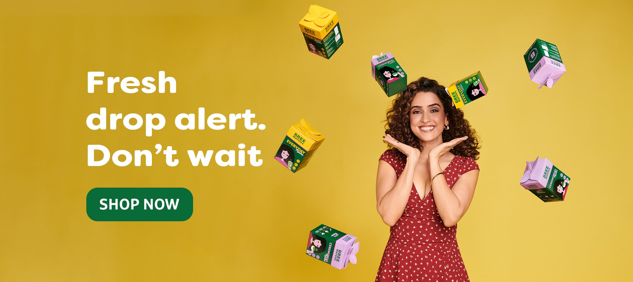 Woman in a red dress surrounded by product boxes with text 'Fresh drop alert. Don't wait' and 'SHOP NOW' on a yellow background.