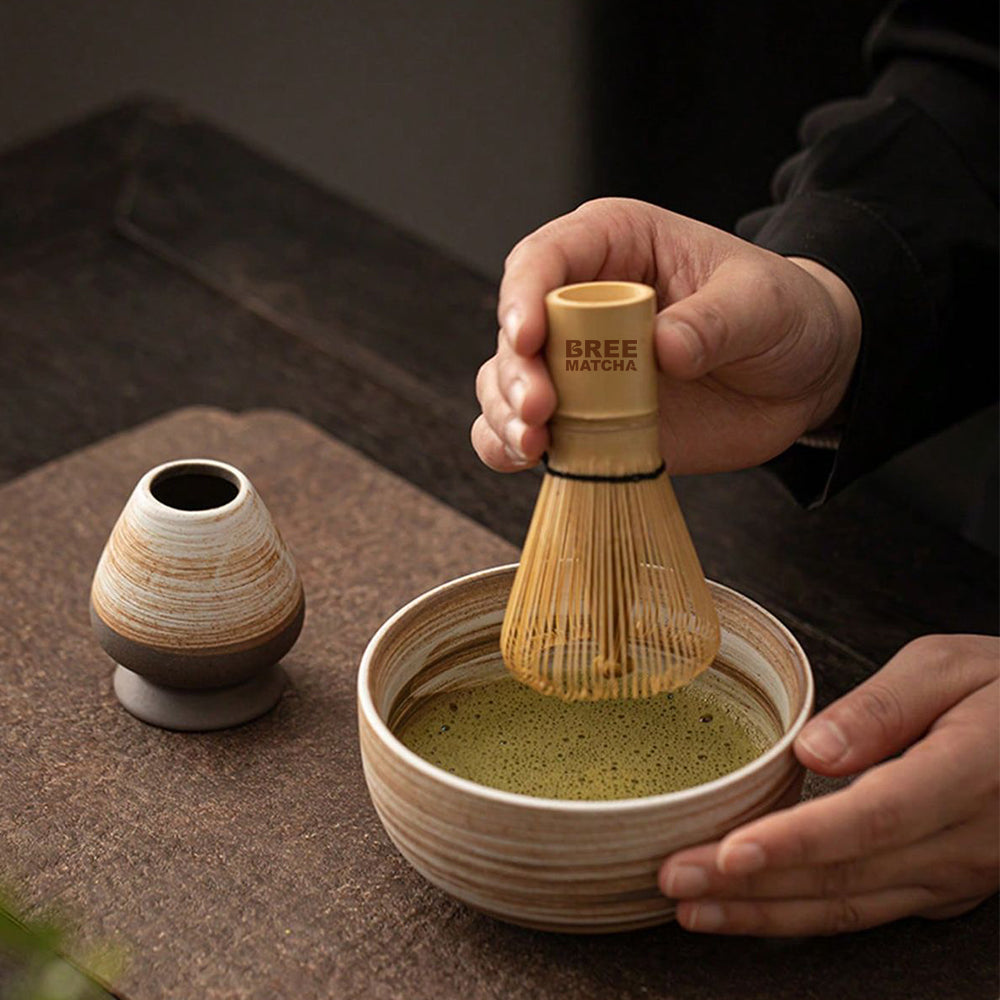 A person uses a matcha whisk to prepare matcha in a ceramic bowl.