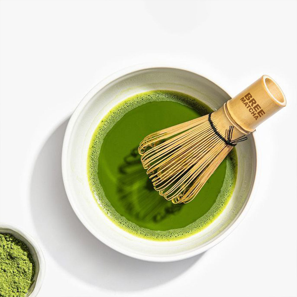 Matcha green tea in a bowl with a bamboo whisk on a white background