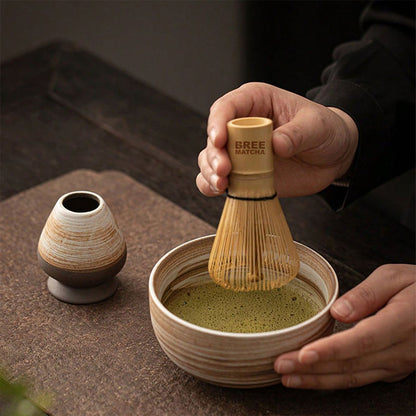 A person uses a matcha whisk to prepare matcha in a ceramic bowl.