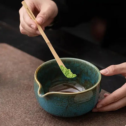 A person uses a matcha whisk to prepare matcha in a ceramic bowl